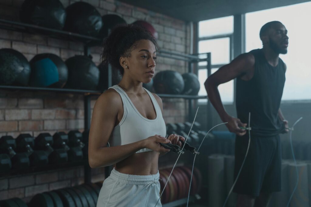 A man and woman in activewear using jump ropes for a workout in a gym setting.